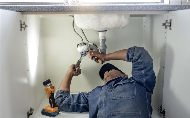 Plumber repairing pipes beneath a bathroom sink in La Quinta
