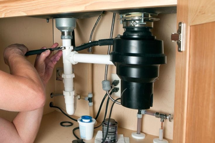 Plumber installing a garbage disposal beneath a kitchen sink in La Quinta