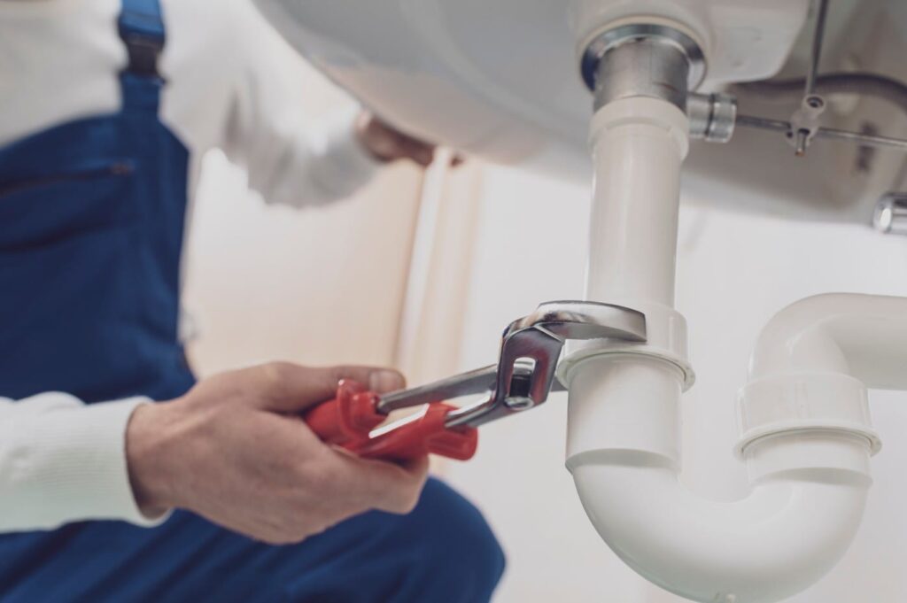 Plumber repairing a white drain pipe beneath a sink in La Quinta