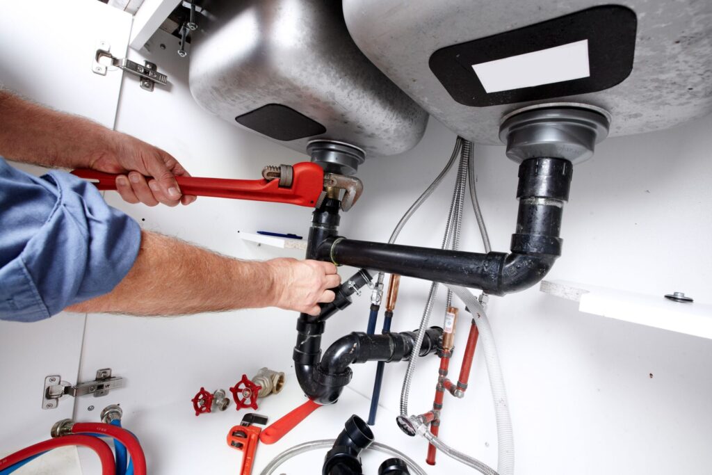 Plumber repairing drain pipes beneath a kitchen sink in La Quinta